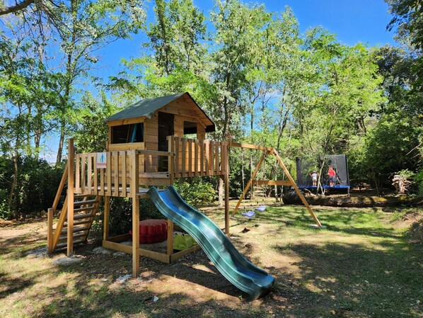 A wooden play structure with a slide and climbing area, surrounded by trees. - Chambre Romarin - Domaine à l'Aise (Saint-Pargoire)