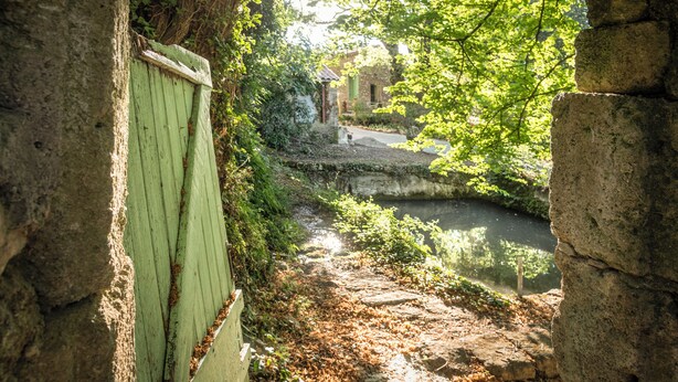 A stone bridge over a small stream, surrounded by greenery and a rustic building. - Chambre Romarin - Domaine à l'Aise (Saint-Pargoire)