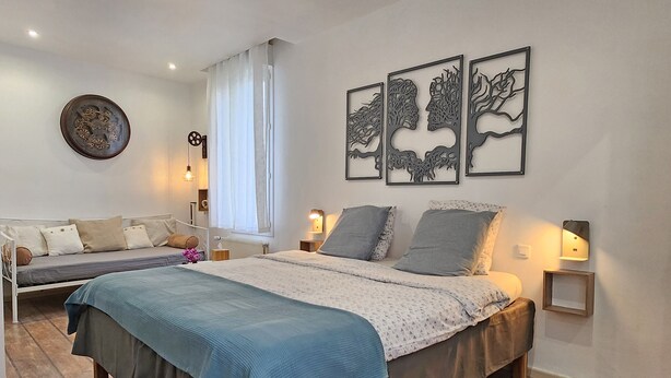 A bedroom with a large bed, a sofa, and a wall-mounted artwork. - Chambre Romarin - Domaine à l'Aise (Saint-Pargoire)