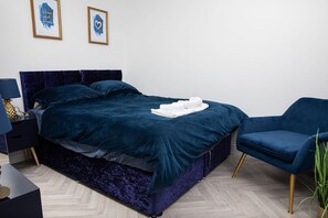 A modern bedroom with a dark blue bedspread, a matching chair, and two framed artworks on the wall. - Apartmentsleeps2-patio-parking-petsok-orpington (Orpington)