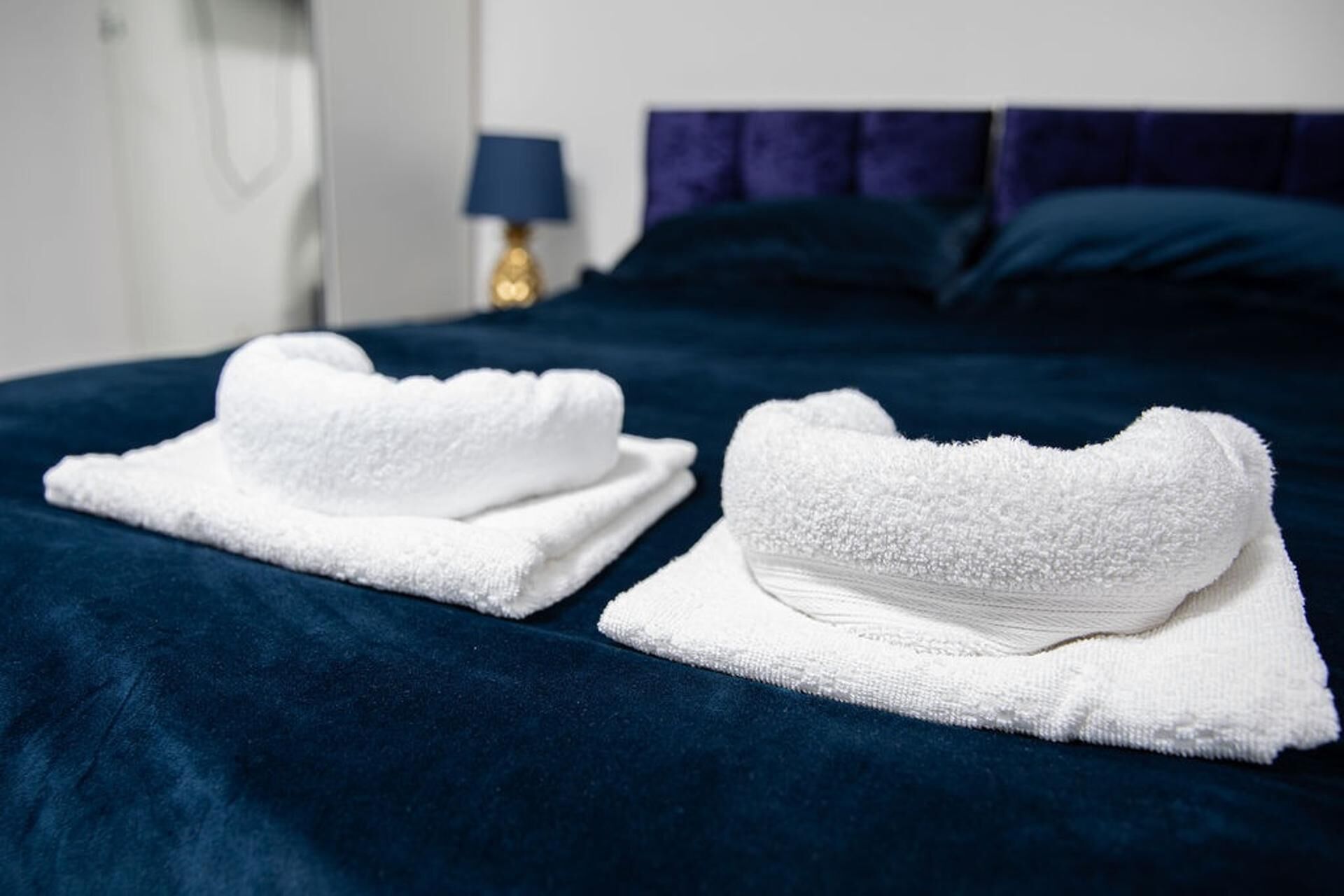 A bed with a dark blue bedspread and two neatly folded white towels placed on it.