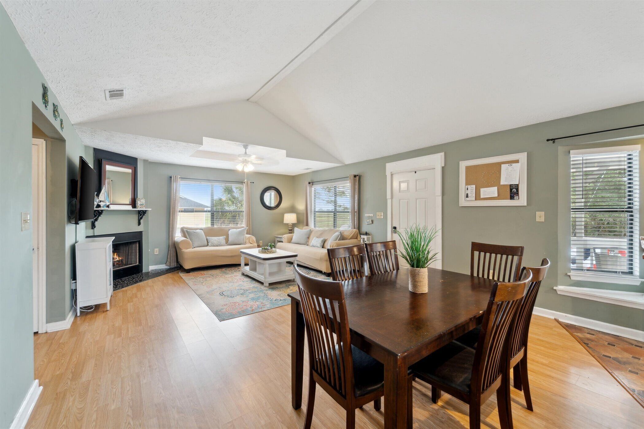 A spacious living room with a fireplace, a dining area with wooden chairs, and a large window with blinds.