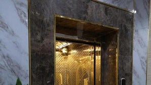 An elevator with a gold interior and a potted plant beside it. - Ansam Taiba Hotel (Madinah)