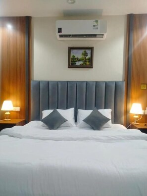 Ein Hotelzimmer mit einem großen Bett, zwei Nachttischlampen, einer Klimaanlage und einem gerahmten Bild an der Wand.