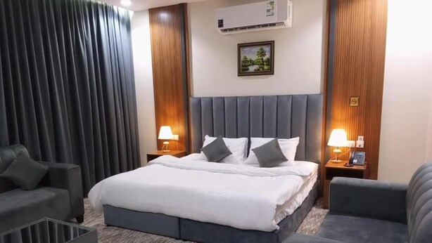 A hotel room with a large bed, two bedside tables with lamps, a grey sofa, and a grey armchair. - Ansam Taiba Hotel (Madinah)