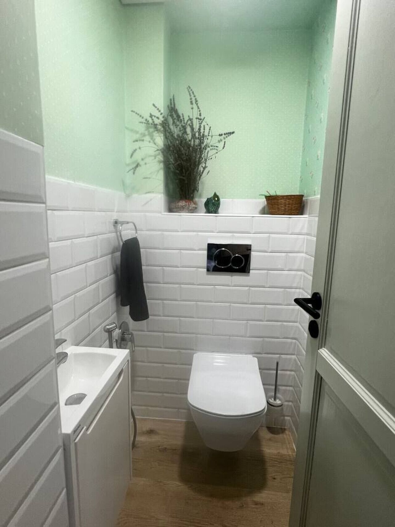 Ein kleines Badezimmer mit weißen Fliesen, Toilette, Waschbecken und einer Zimmerpflanze an der Wand.
