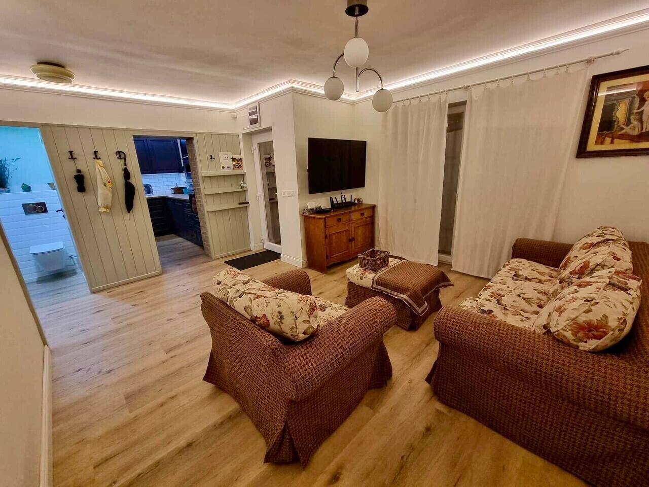A living room with a sofa set, a television, and a dining area visible through an open door.