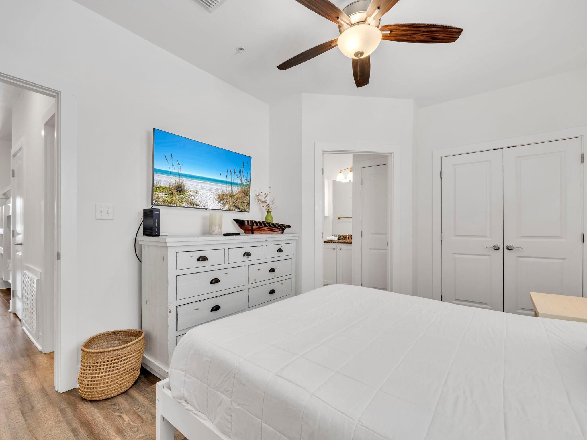 A bedroom with a bed, a ceiling fan, a TV, a dresser, and a door.