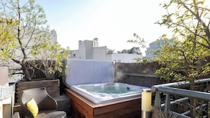 Een terras op het dak met een jacuzzi, rieten stoelen en een houten terras.