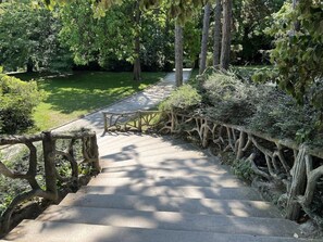 A stone staircase with a rustic wooden railing, surrounded by lush greenery and trees. - Les Résidences Lavaud (Paris)