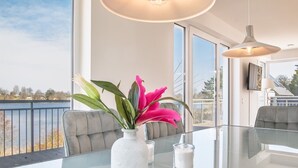 A modern dining area with a glass table, a vase with flowers, and a view of the outdoors. - House Langsee 2 (Kosel)