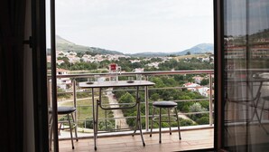 A balcony with a table and two chairs, overlooking a town with houses and hills. - SELÇUK APART (Gökçeada)