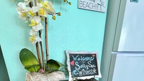 A wooden table with a chalkboard sign reading "Welcome to Sandy Sea Witches' Cove," a small decorative plant, and a sign saying "Feeling BEACHY." - Salty Sea Wishes - Ocean Views, Beach Access, Family Vibes (Galveston)