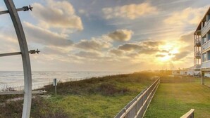 A wooden boardwalk leading to a beach with a sunset in the background. - Salty Sea Wishes - Ocean Views, Beach Access, Family Vibes (Galveston)