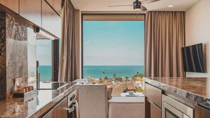 A modern kitchen with a large window overlooking the ocean, a ceiling fan, and a flat-screen TV mounted on the wall. - Arbor at Caivama (Sayulita)