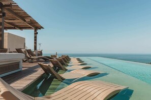 Ein Poolbereich mit Liegestühlen und einer Holzpergola mit Blick aufs Meer.