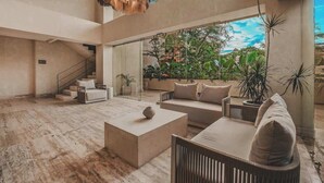 A spacious living area with a high ceiling, a staircase, and a view of lush greenery outside. - Arbor at Caivama (Sayulita)