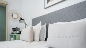 A neatly made bed with white bedding and a pillow with the word "embrace" embroidered on it. - GuestReady - Zenith Building - Room 002 (Porto)