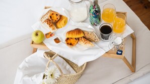 A breakfast tray with pastries, a jug of milk, orange juice, and tea on a bed. - GuestReady - Zenith Building - Room 002 (Porto)