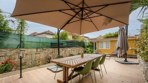 An outdoor patio with a wooden table and chairs, a large umbrella, and a garden with flowers and a fence. - GuestReady - Zenith Building - Room 001 (Porto)