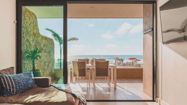 Une chambre dotée d’une grande porte-fenêtre coulissante donnant sur un balcon avec vue sur la plage et l’océan.