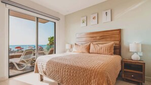 Une chambre avec un grand lit, une table de chevet et une vue sur la plage, accessible par une porte coulissante.