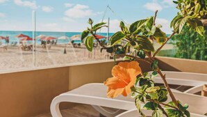 Un balcon avec vue sur la plage, des chaises longues blanches et un hibiscus.
