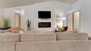 Una sala de estar moderna con un televisor de pantalla plana montado en una pared blanca, una chimenea debajo y un área de estar acogedora con un sofá y sillones.