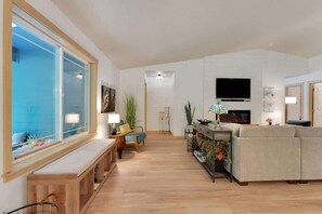 Ein modernes Wohnzimmer mit großem Fenster, einer Couch, einem Fernseher und einer hölzernen Bank.