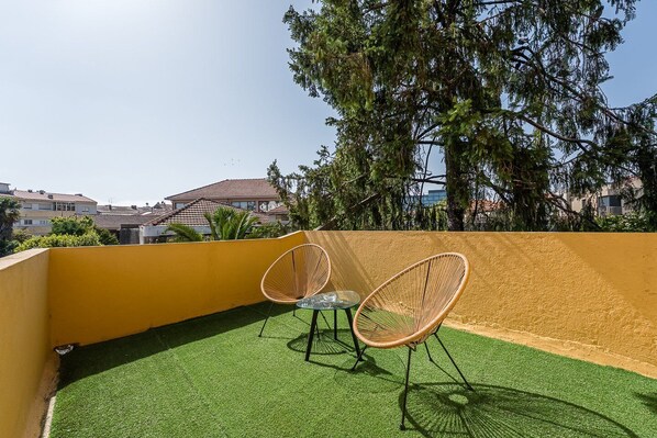 A rooftop terrace with artificial grass, two wicker chairs, and a yellow wall.