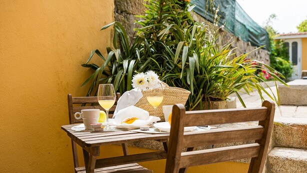 A wooden table set with a white cloth, two glasses of white wine, a white mug, and a basket of bread. - GuestReady - Zenith Building - Room 102 (Porto)