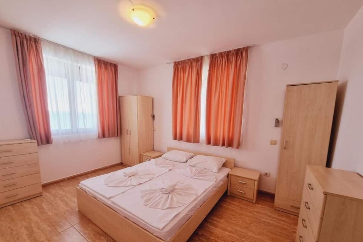 A bedroom with a wooden bed, two nightstands, a wardrobe, and a window with curtains.