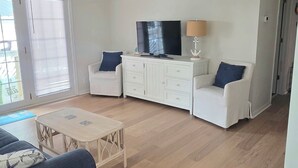 Amplia sala de estar con televisor de pantalla plana, muebles blancos y ventilador de techo.