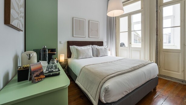 Une chambre d’hôtel avec un lit, un bureau avec une carte et une télécommande, une lampe et une fenêtre avec des rideaux.