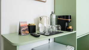 Une chambre d’hôtel avec un comptoir vert, une carte de la ville encadrée, une machine à café, un distributeur d’eau et une télécommande.