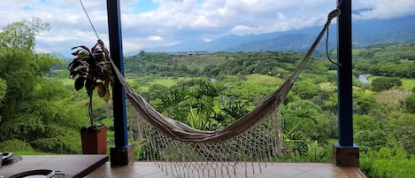 Un hamac sur un balcon donnant sur un paysage luxuriant, avec des montagnes à l'horizon.