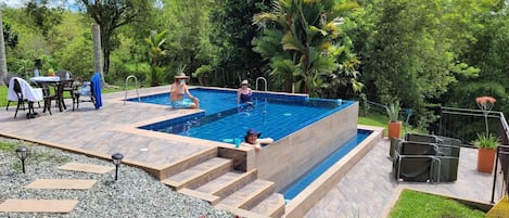 A rectangular swimming pool with steps leading into it, surrounded by outdoor furniture and potted plants.