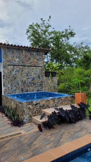 A stone building with a swimming pool, surrounded by plants and trees.