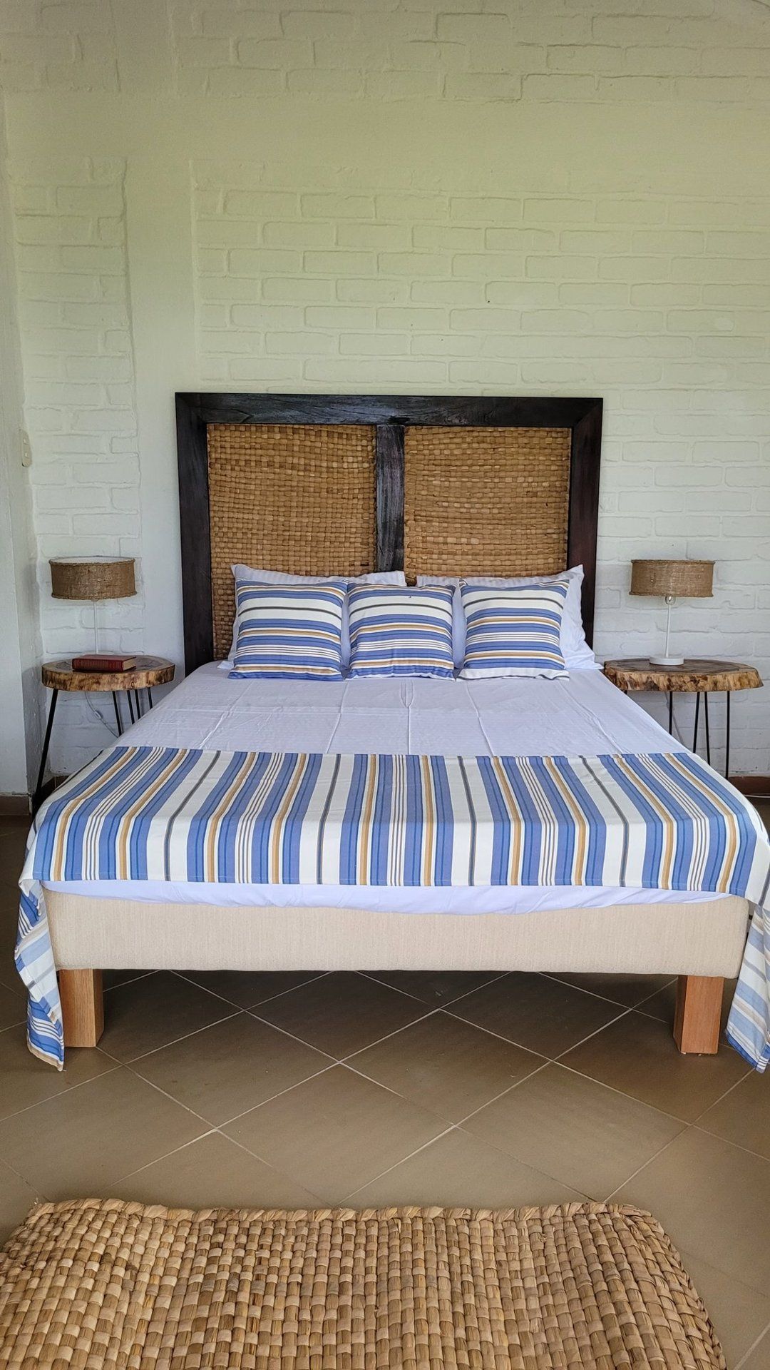 A bed with a striped bedspread, a woven headboard, and two bedside tables with lamps.