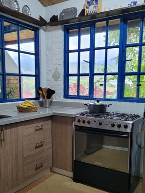 A kitchen with a stove, a window with a view of greenery, and a basket of bananas on the counter.