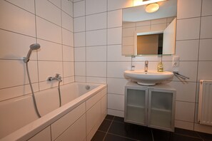 A modern bathroom with a bathtub, a sink with a mirror above it, and a cabinet below. - Residence Alpin TOP 1 incl SUMMER CARD (Kaprun)