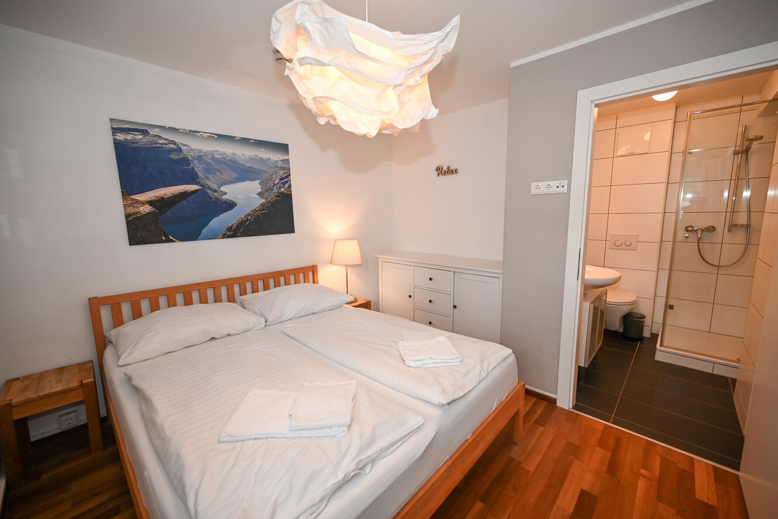 Et soveværelse med seng, sengebord, lampe samt et badeværelse med bruser og toilet.