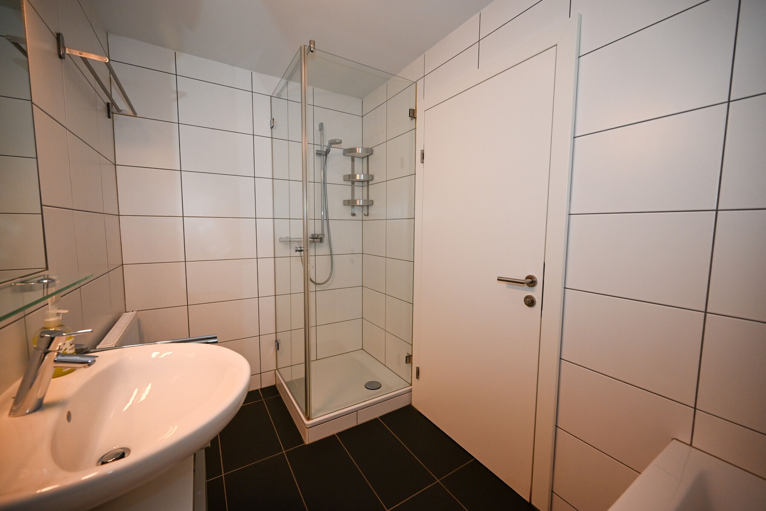 A bathroom with a white sink, glass-enclosed shower, and tiled walls.