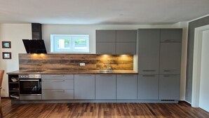 A modern kitchen with grey cabinets, a wooden countertop, a built-in oven, and a window above the sink.