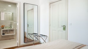 A bedroom with a bed, a large mirror, a door, and a bathroom with a sink and mirror. - GuestReady - Zenith Building - Room 201 (Porto)