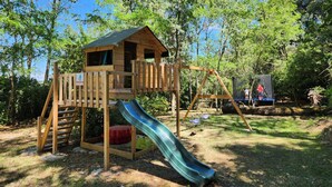 Una estructura de fusta per jugar amb tobogan i zona d'escalada, envoltada d'arbres.