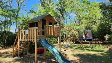 A wooden play structure with a slide and climbing area, surrounded by trees.