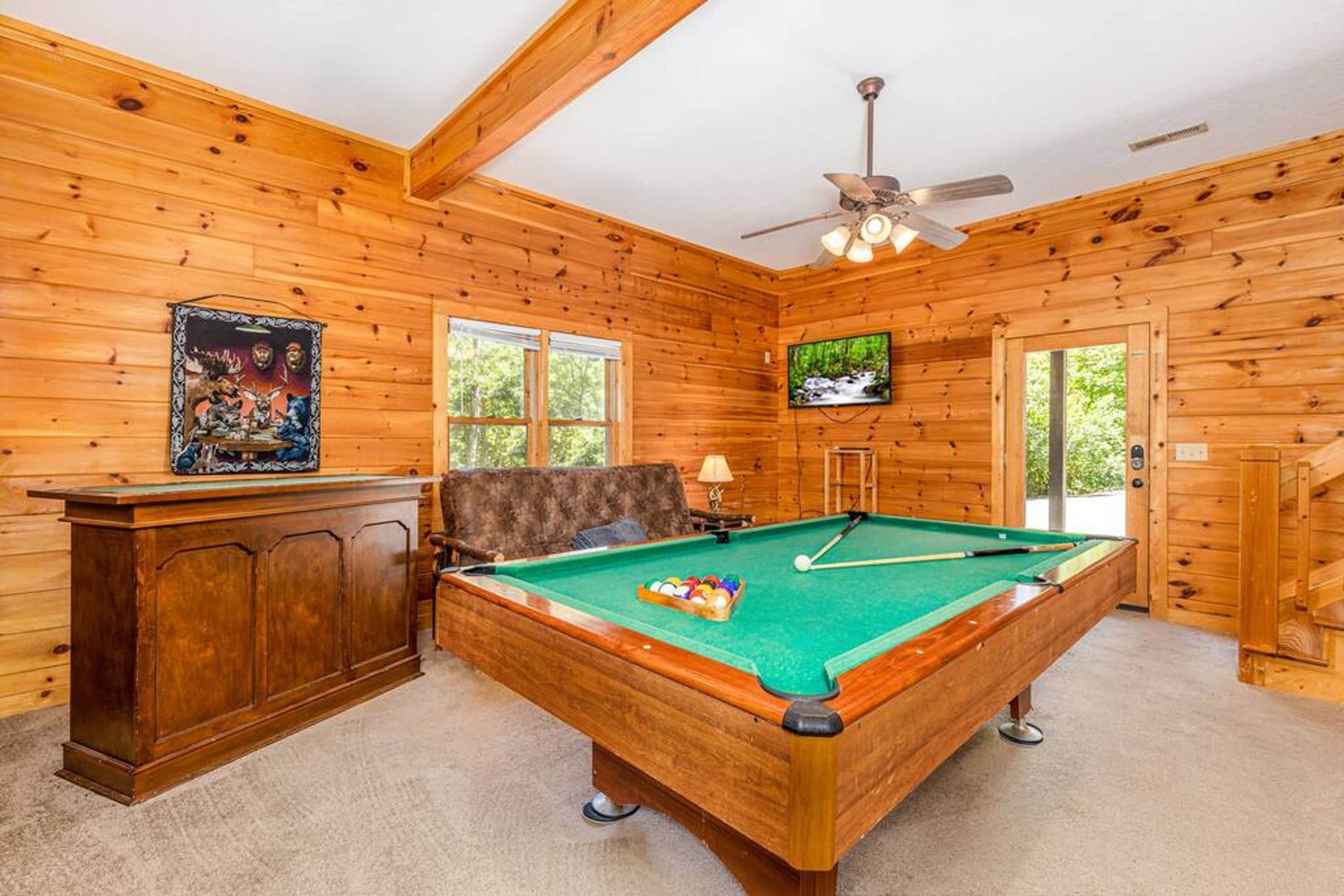 A wooden-paneled room with a pool table, a television, and a ceiling fan.