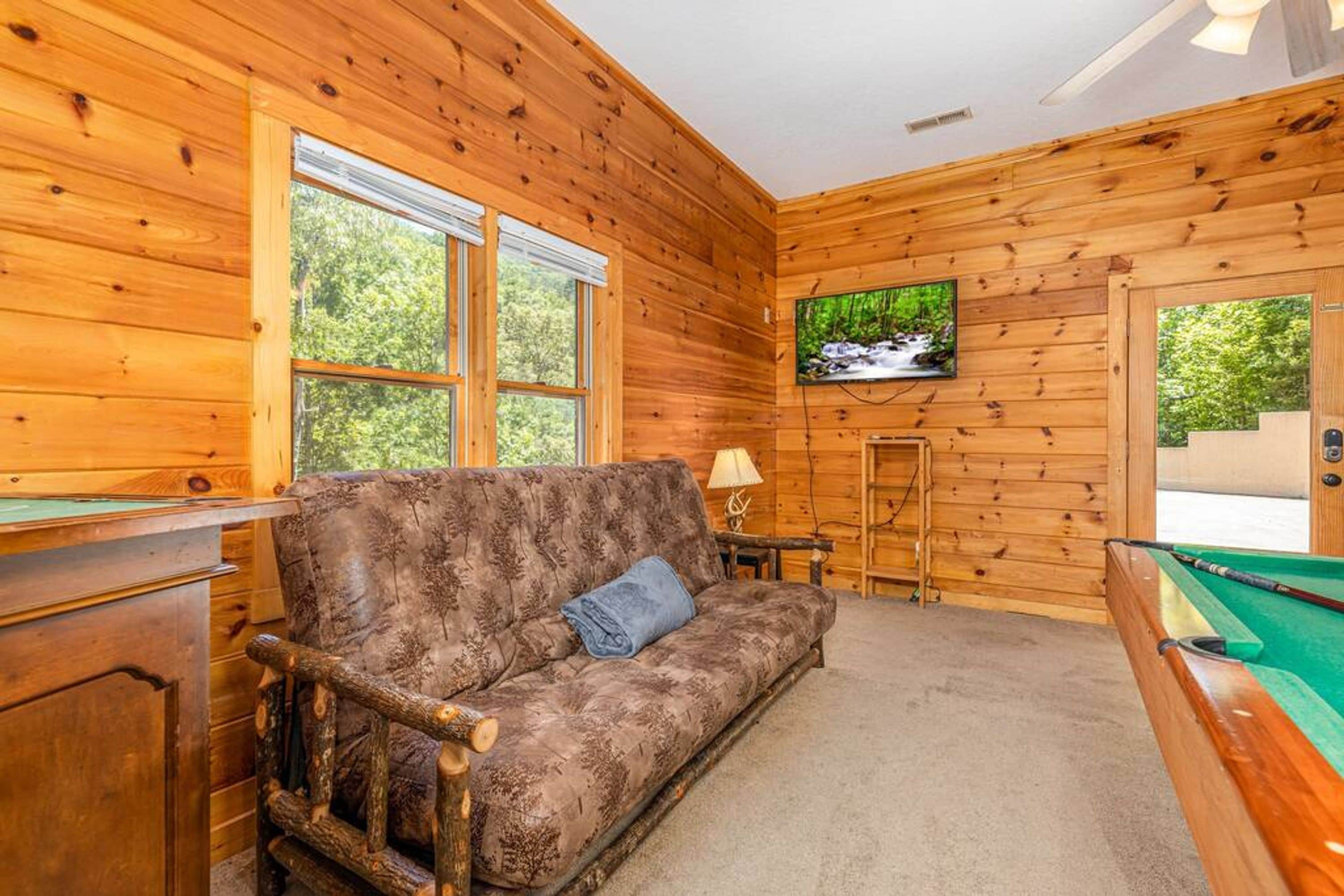 A cozy room with a wooden wall, a sofa, a pool table, and a television.