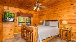 A wooden cabin bedroom with a bed, a TV, a window, and a ceiling fan. - Secluded 3BR Cabin w Hot Tub Dog Friendly Sleeps12 (Pigeon Forge)